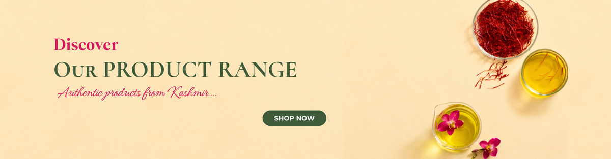 A promotional banner on a pale yellow background featuring the text 'Discover Our Product Range: Authentic products from Kashmir' above a dark green 'Shop Now' button. On the right, there is a glass bowl filled with red saffron threads alongside small glass beakers containing golden oil and a bright pink orchid flower.